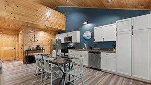 Une cuisine moderne avec un plafond en bois, des armoires blanches, des appareils électroménagers en acier inoxydable et un coin repas avec des chaises blanches.