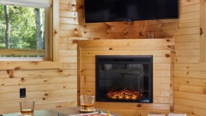 L’intérieur d’un chalet accueillant, avec une cheminée, des murs en bois, un téléviseur et une table où sont disposés des collations et des boissons.