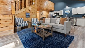 L’intérieur chaleureux d’un chalet avec un escalier en bois, un coin repas, une cuisine et un salon comprenant un canapé et des fauteuils à rayures.