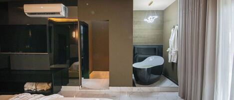 A modern hotel room with a large bed, a built-in wardrobe, a bathroom with a bathtub, and a mirror reflecting the room.