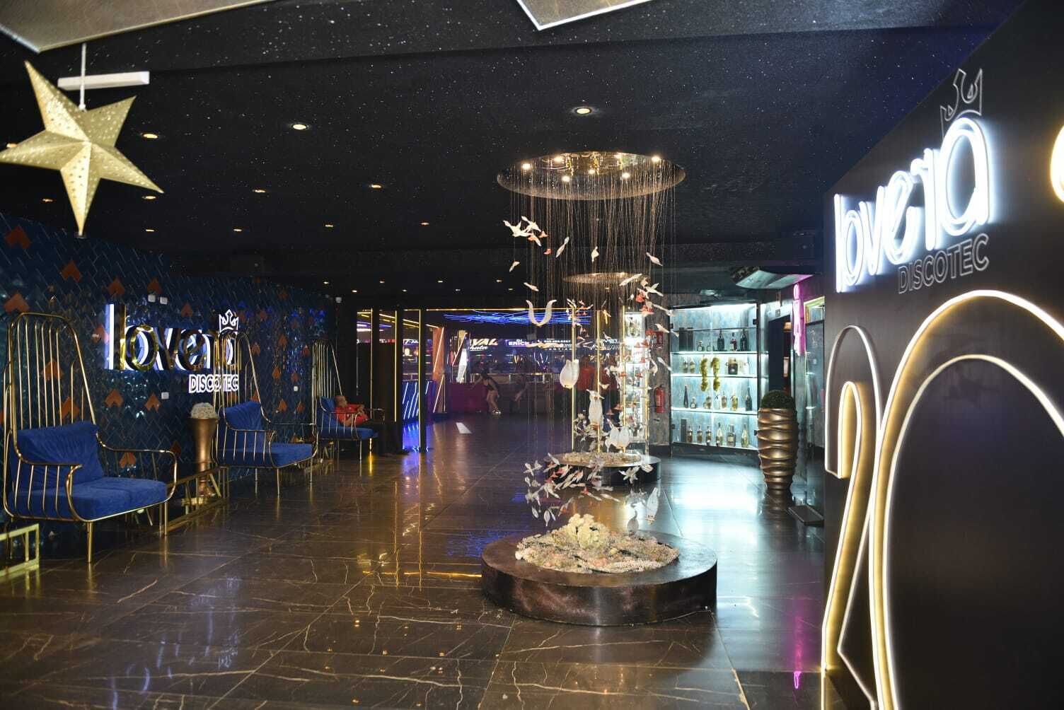Un interior moderno con una fuente decorativa central, zonas de estar con sillas azules y una tienda visible llamada 'bovio DISCOTECS'.