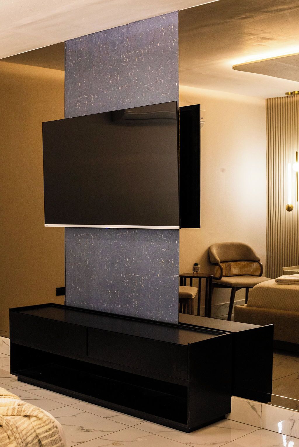 A modern living room with a flat-screen TV mounted on a black entertainment unit, a sofa, and a chair.