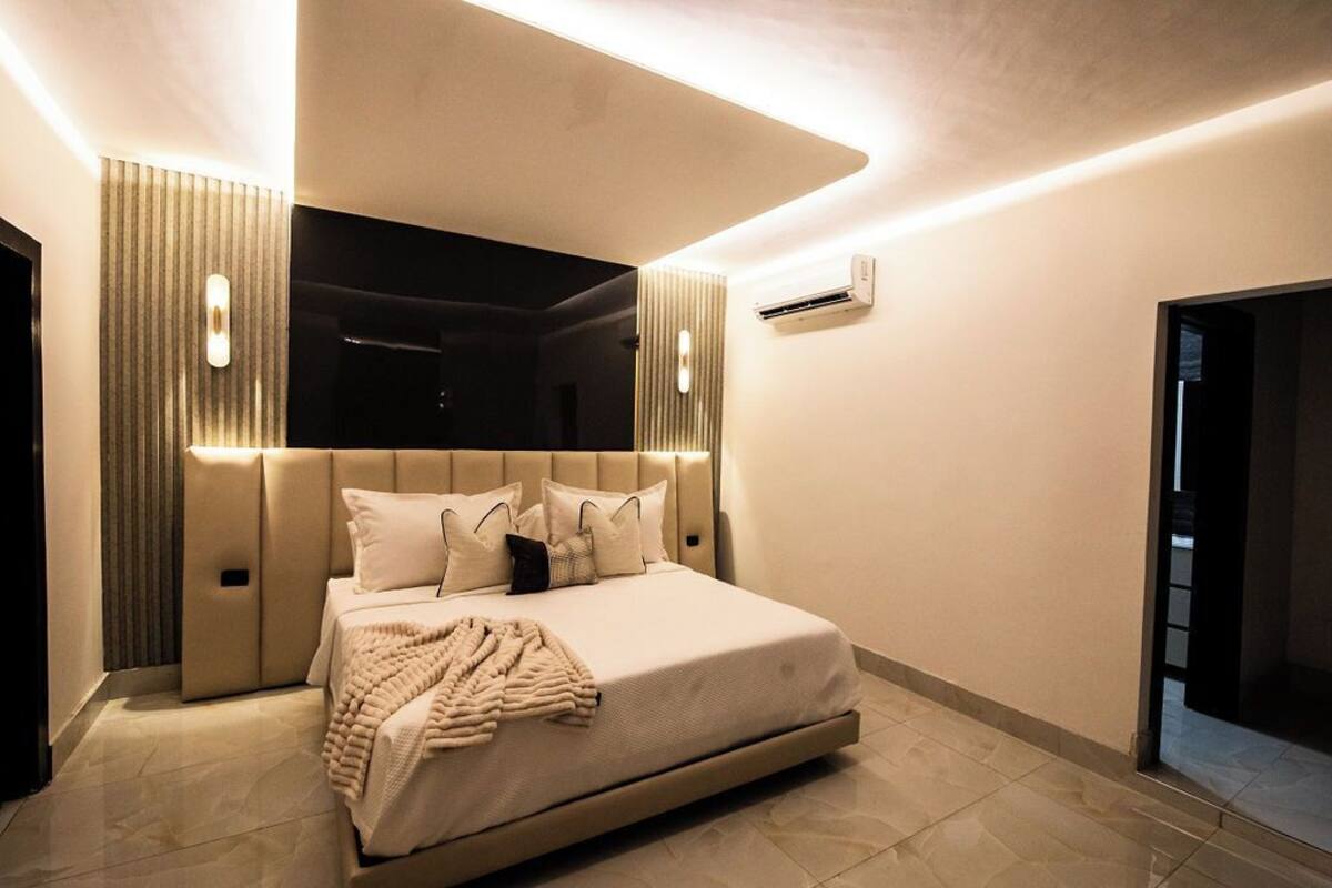 Un dormitorio moderno con una cama grande, una mesita de noche, aire acondicionado de pared y un espejo.