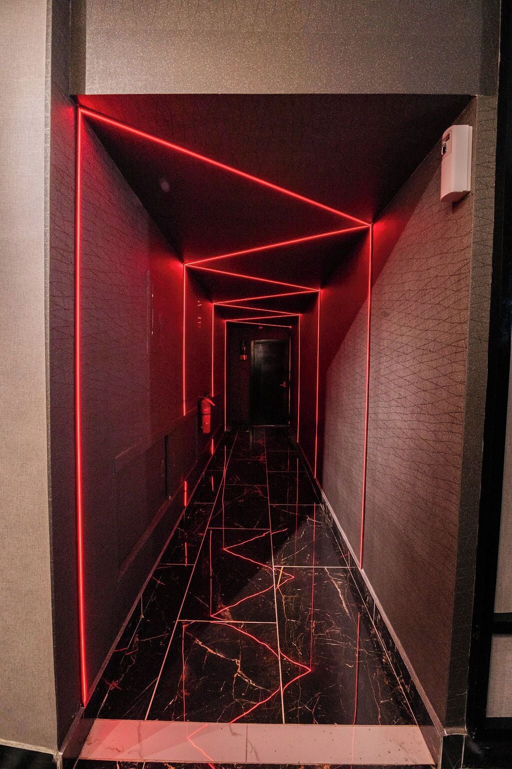 A corridor with red neon lighting, a fire extinguisher, and a textured wall.