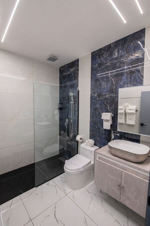 A modern bathroom with a glass-enclosed shower, a toilet, a sink with a marble countertop, and a vanity with a mirror. - Lovera Hotel (Santiago de los Caballeros)