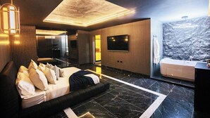 Un dormitorio moderno con una cama grande, un televisor de pantalla plana, una bañera integrada y una pared con textura de piedra.