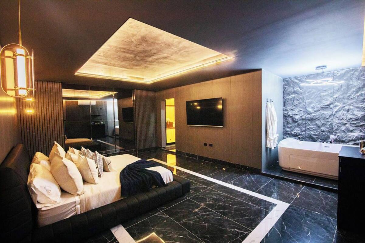 Un dormitorio moderno con una cama grande, un televisor de pantalla plana, una bañera integrada y una pared con textura de piedra.