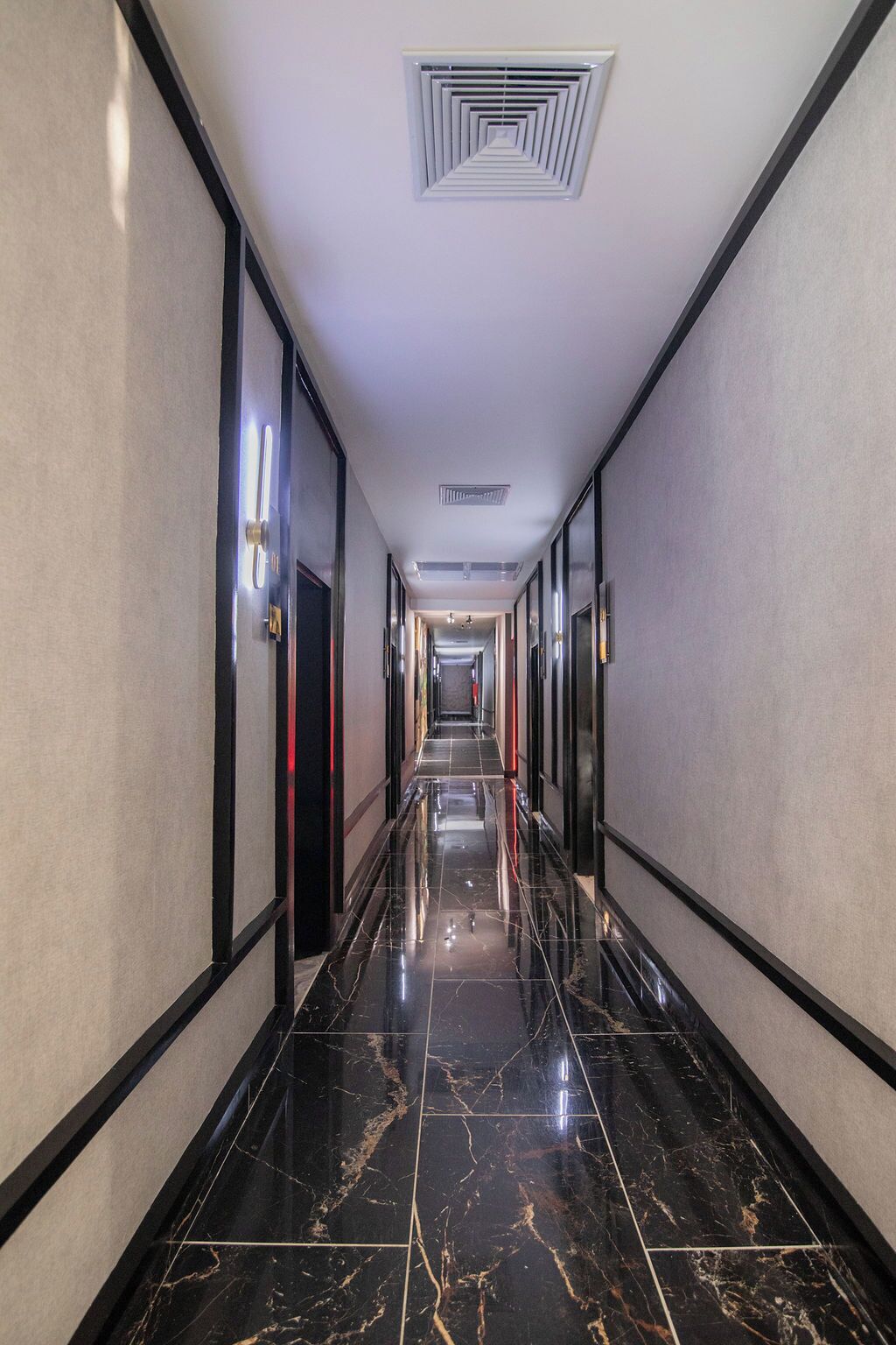 A long, narrow hallway with a glossy black marble floor, white walls, and a ceiling vent.