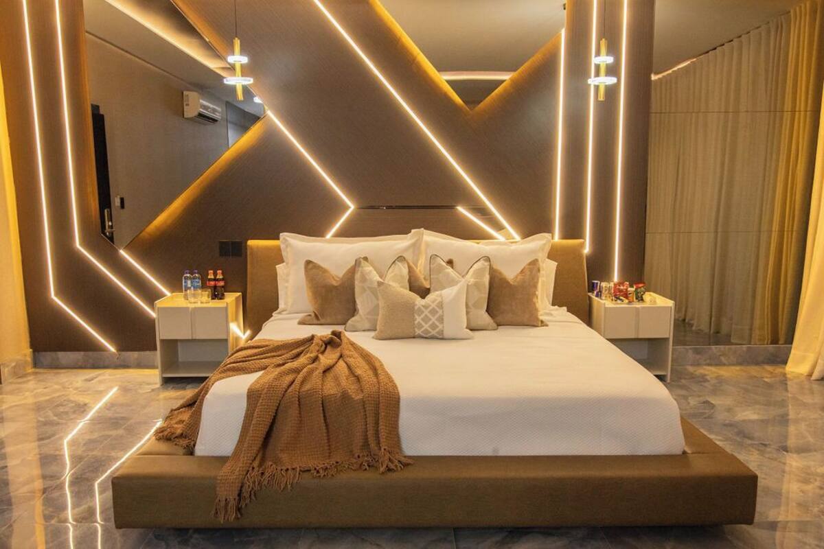 Un dormitorio moderno con una cama grande, iluminación de pared geométrica y suelo de mármol.