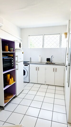 Een moderne keuken met witte kasten, een inbouwoven, een wasmachine en een raam met uitzicht.
