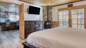 Een kamer met een groot bed, een houten plafond, een stenen open haard, een aan de muur bevestigde televisie en een vluchtroute indicator.