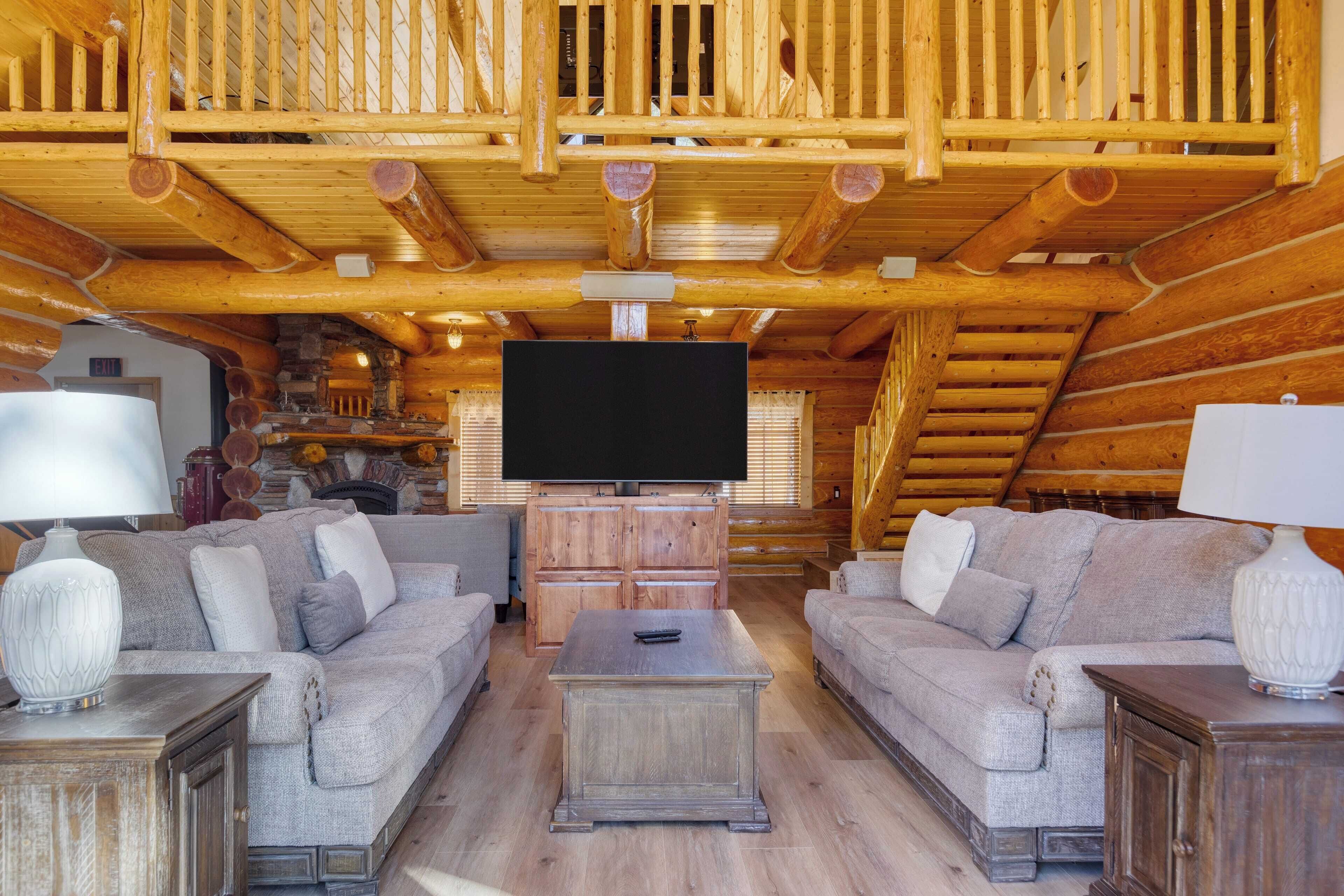 A log cabin interior with a wooden ceiling, two sofas, a television, and a fireplace.