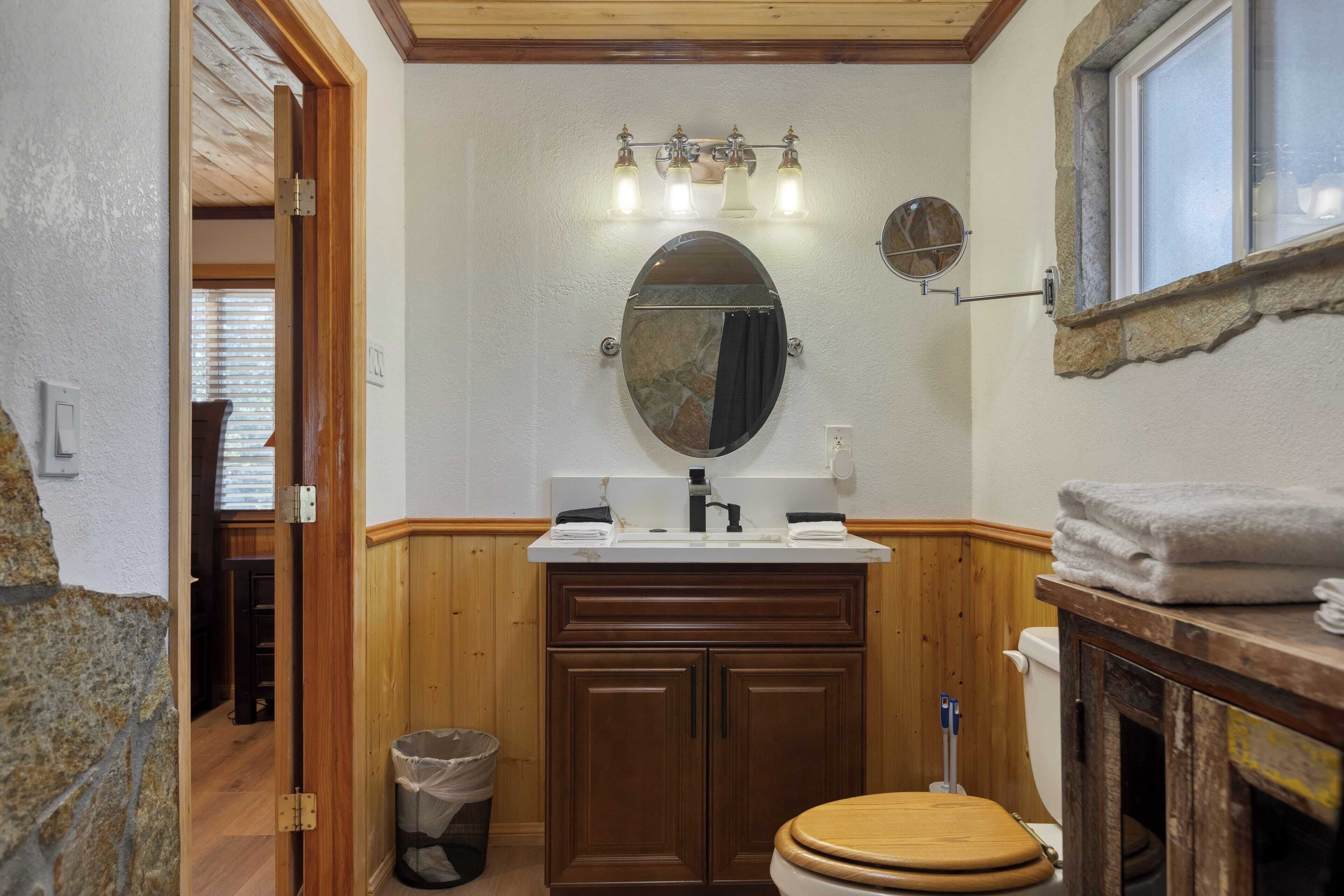 A bathroom with a wooden vanity, a toilet, a sink with a mirror, and a window with a stone frame.