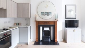 Una cocina moderna con armarios de madera clara, encimera blanca, horno empotrado y chimenea negra con repisa.
