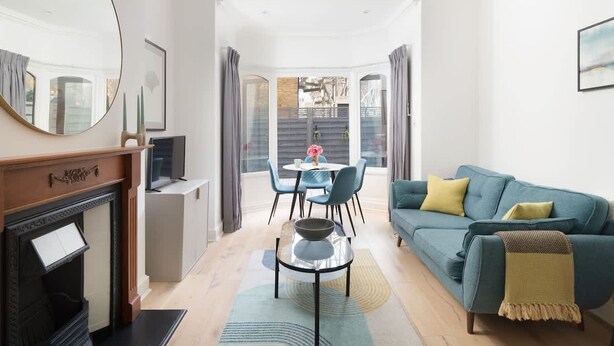 Una sala moderna con un sofá azul, una chimenea, una mesa de comedor con sillas y un espejo grande.