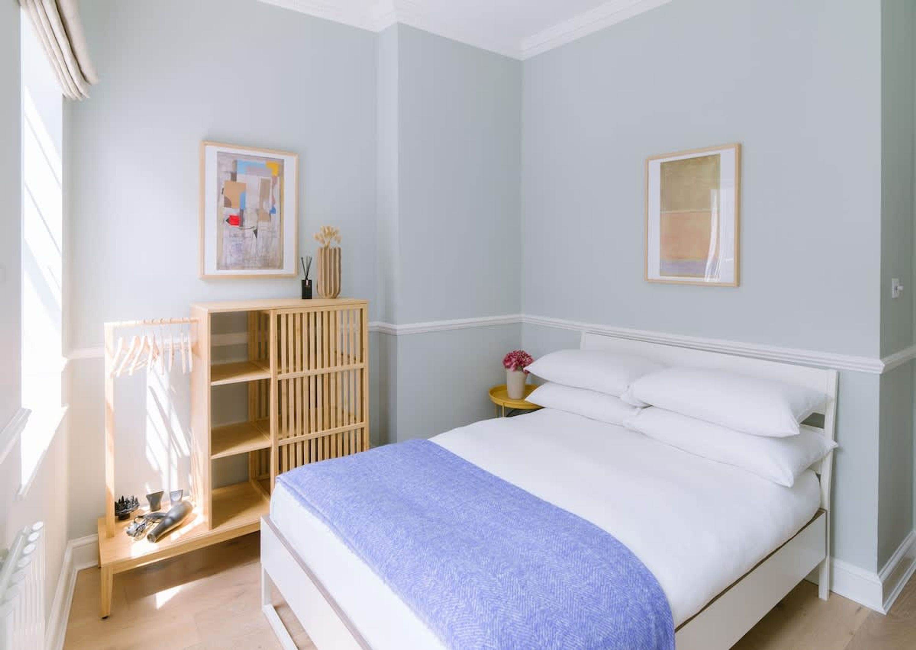 Een slaapkamer met een bed, een houten garderobe, een nachtkastje en twee ingelijste foto's aan de muur.