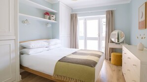 Un dormitorio con cama, cómoda, espejo y ventana con cortinas.