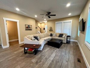 A living room with a sectional sofa, a coffee table, a ceiling fan, and a TV mounted on the wall.