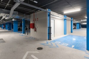 Un estacionamiento de varios niveles con pilares azules, paredes blancas y flechas direccionales en el suelo.