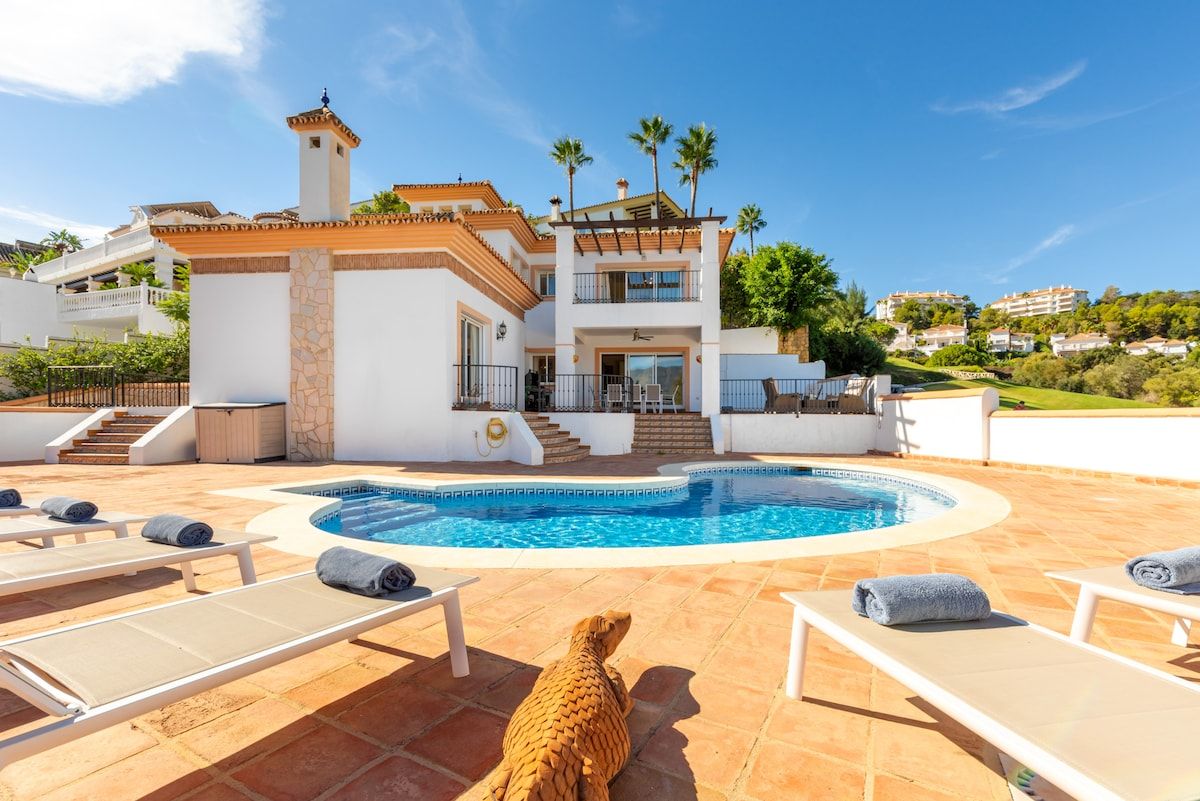 A two-story villa with a swimming pool, outdoor seating, and a dog.