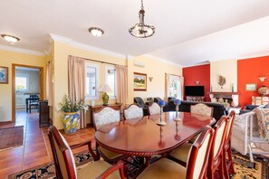 A dining area with a round table, chairs, and a chandelier. There is a living room with a sofa and a fireplace.