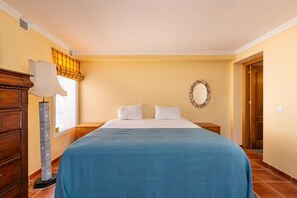 A bedroom with a bed, a dresser, a nightstand, a wall mirror, and a window with a curtain.