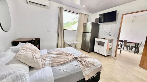 Una habitación de hotel con cama, escritorio, refrigerador, televisor y ventana con cortinas.