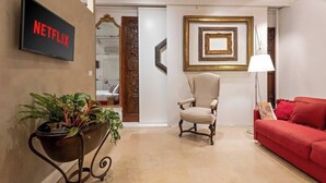 A modern living room with a red sofa, a beige armchair, a potted plant, a wall-mounted TV, and framed artwork. - Luxurious home of the antiquarian at Spanish Steps (Rome)