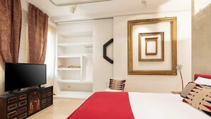 A modern hotel room with a large bed, a flat-screen TV, a wardrobe, and a built-in shelving unit. - Luxurious home of the antiquarian at Spanish Steps (Rome)