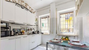 A modern kitchen with white cabinets, a microwave, and a dining area with clear chairs and a glass table. - Luxurious home of the antiquarian at Spanish Steps (Rome)