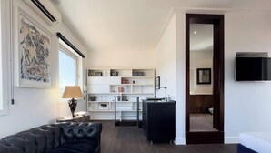 A modern living room with a black leather sofa, a blue armchair, and a kitchen area with white cabinets and a black countertop. - Chasing the Stars Spanish Steps Boutique Suite (Rome)
