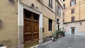 A building with a large wooden double door, a small window with metal bars, and a potted plant outside. - Chasing the Stars Spanish Steps Boutique Suite (Rome)