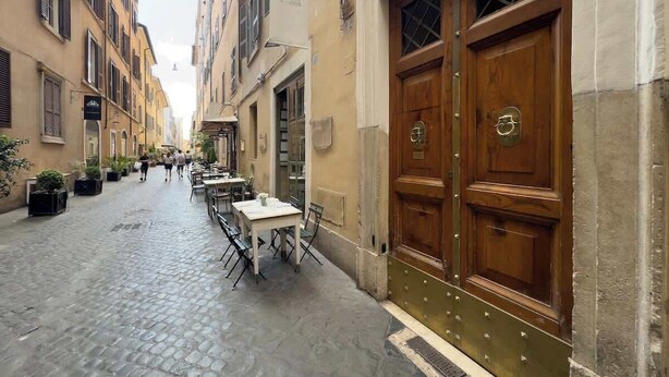 A narrow cobblestone street with outdoor seating, wooden doors, and buildings with multiple stories. - Chasing the Stars Spanish Steps Boutique Suite (Rome)
