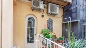 A building with a beige facade, a white door, and a balcony with potted plants.