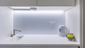 A modern kitchen with a white countertop, a stainless steel faucet, a kettle, and a bowl of tea bags.