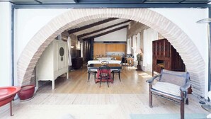 A spacious dining area with a long table and chairs, an arched brick structure, and a view into a kitchen area.