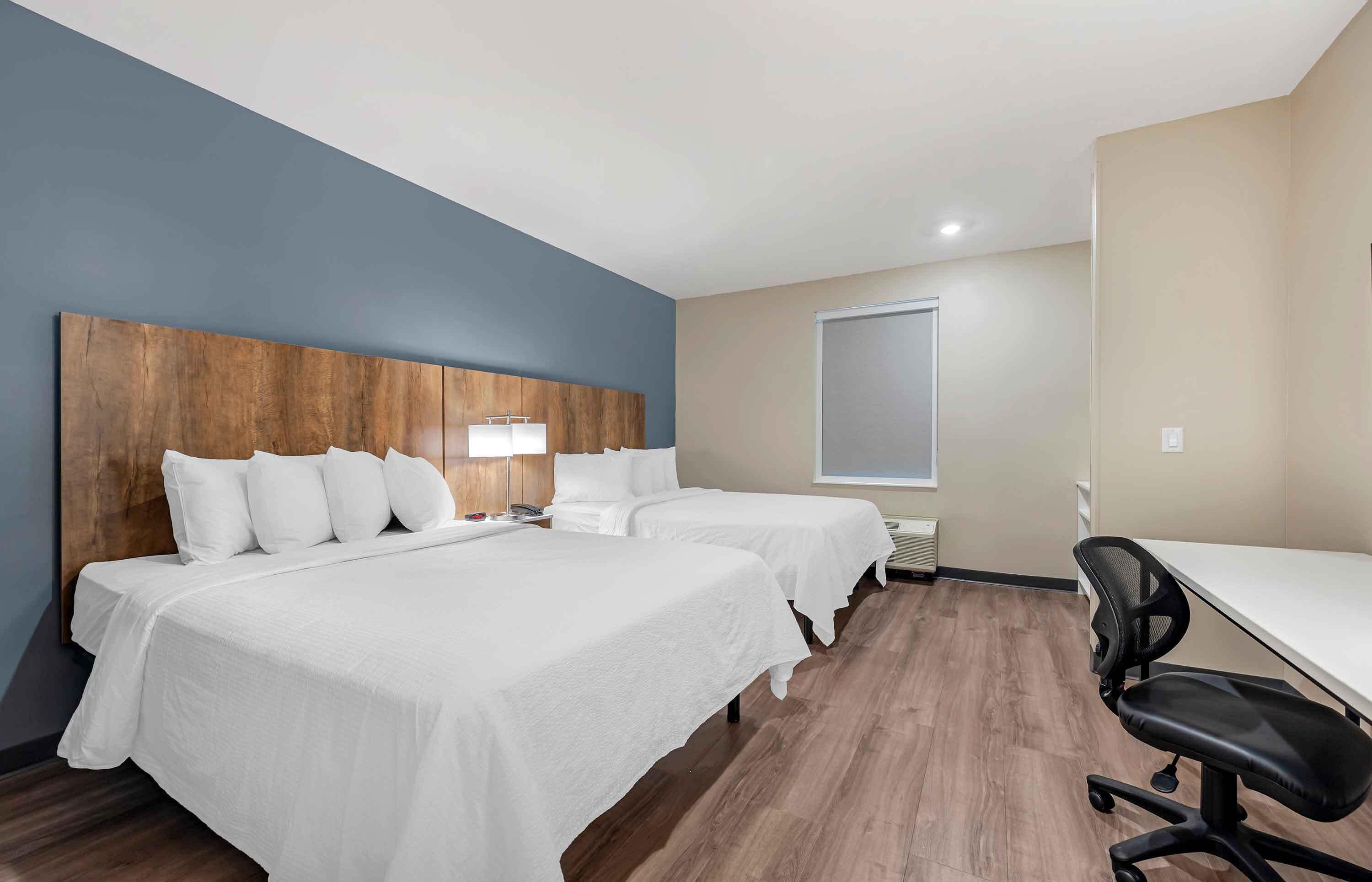 Een hotelkamer met twee bedden, een bureau, een stoel en een raam.