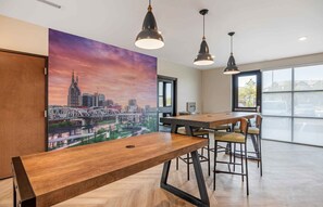 Una sala de reuniones moderna con un gran cuadro de un paisaje urbano, mesas de madera e iluminación colgante.