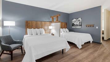Habitación de hotel con dos camas, una silla, una mesita de noche, una lámpara y un perchero en la pared.