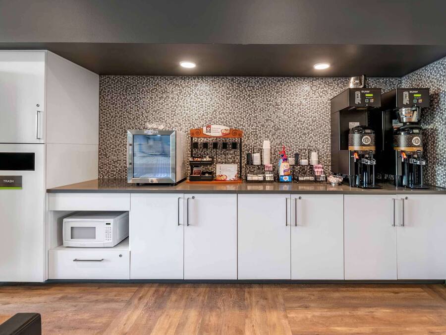 Una cocina moderna con microondas, cafeteras y un cubo de basura.