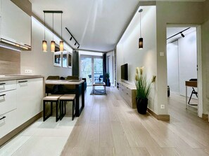 A modern kitchen with a dining area, a TV mounted on the wall, and a potted plant.