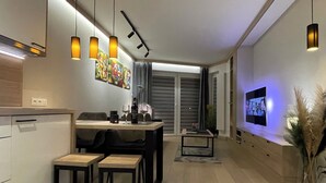 Eine moderne Küche mit Pendelleuchten, ein Essbereich mit Tisch und Stühlen, ein an der Wand montierter Fernseher und ein Blumentopf.