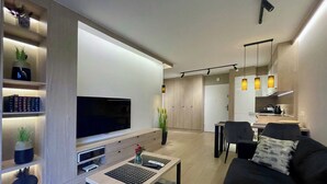 Ein modernes Wohnzimmer mit Flachbildfernseher, Couchtisch, Sofa und Essbereich mit Stühlen.