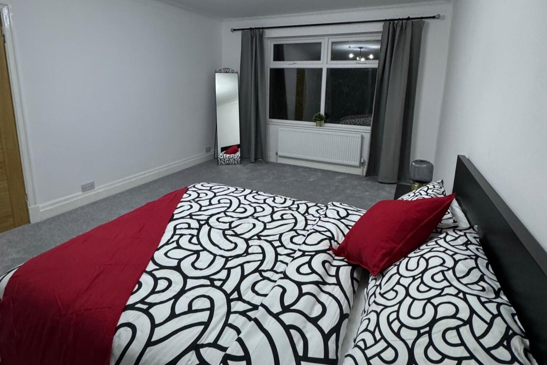 Een slaapkamer met een bed, een raam, een radiator en een spiegel.