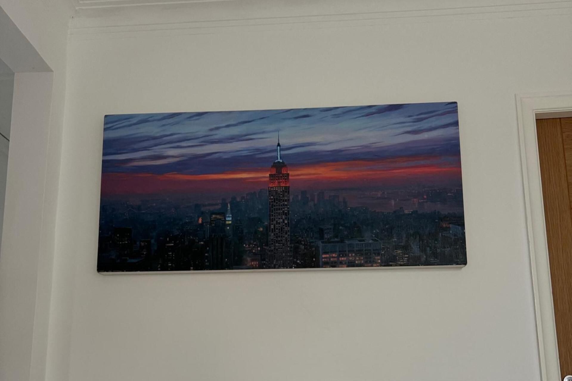 A cityscape painting with a prominent skyscraper, likely the Empire State Building, against a twilight sky.