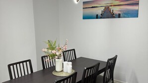 A dining area with a dark wooden table, black chairs, a vase with flowers, and a wall-mounted picture of a sunset over a pier.