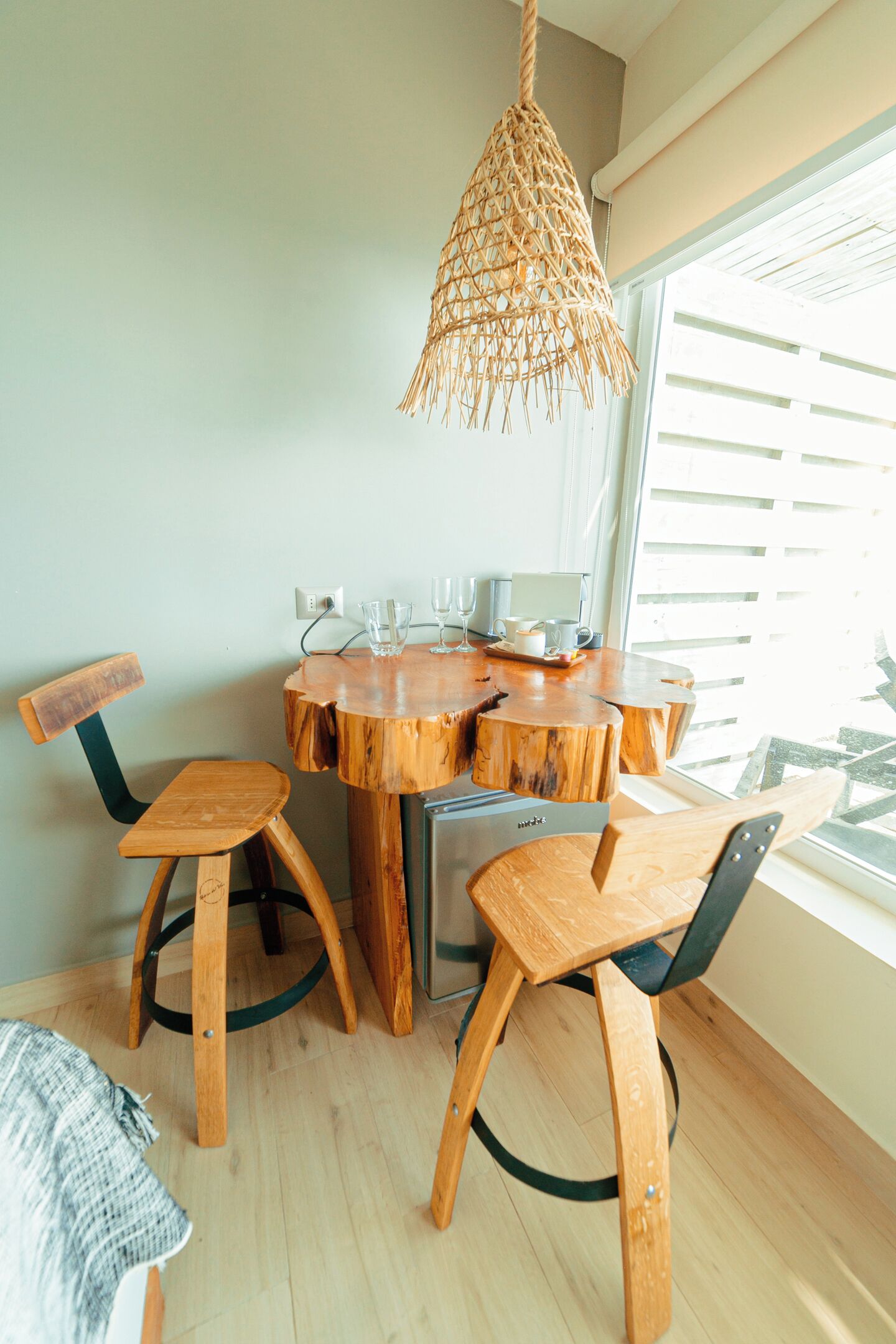 A wooden dining table with chairs, a hanging light fixture, and a window with blinds.