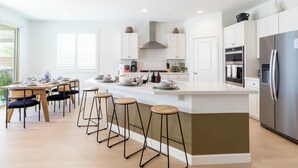 A modern kitchen with a central island, bar stools, and a dining area with a table and chairs.