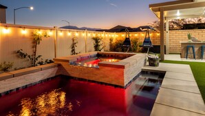 A backyard with a swimming pool, a barbecue area, and string lights.