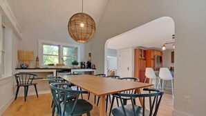 Un vaste espace dédié à la salle à manger, avec une table en bois et des chaises modernes, un luminaire suspendu et une vue sur la cuisine.